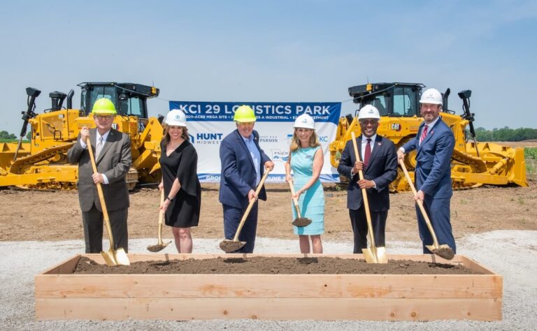 Officials in hard hats and business attire pose with shovels of dirt in front of bulldozers and a banner for KCI 29 Logistics Park.