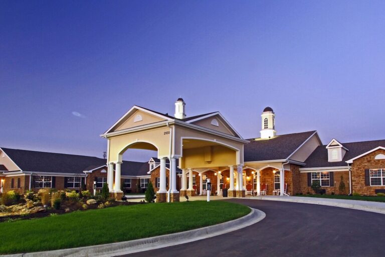 Elegant one-story brick and siding building with white columns, covered entryway, and cupolas, lit warmly at dusk with landscaped grounds.