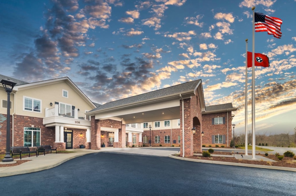 Two-story brick building with white trim and a large covered driveway entrance, lit warmly beneath a dramatic cloudy sunset sky.