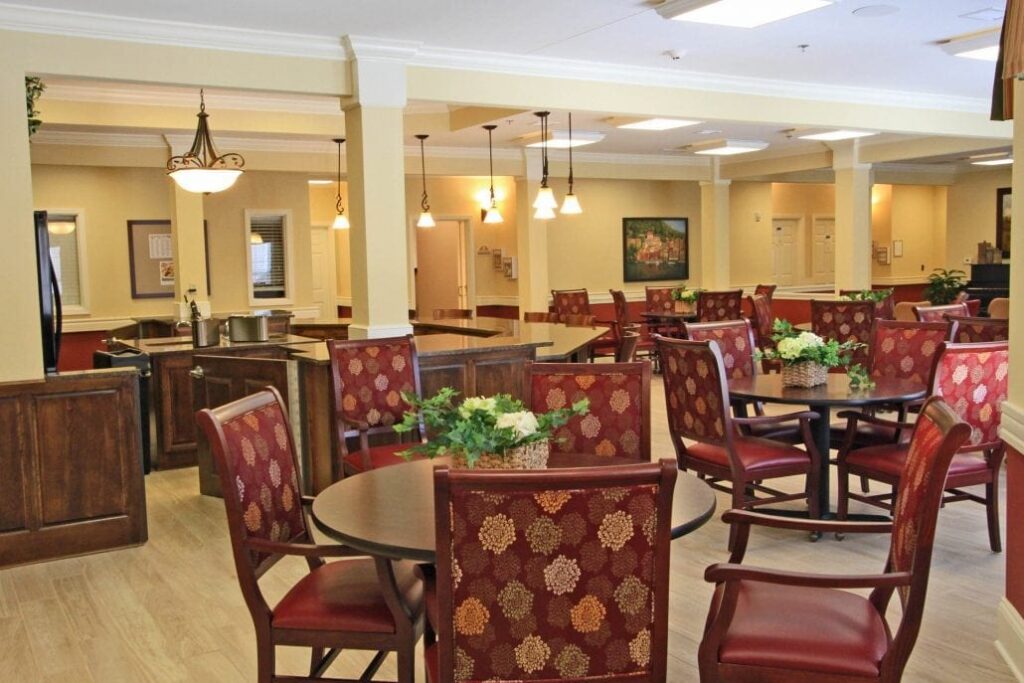 Spacious dining area with round tables, red patterned chairs, pendant lighting, and potted greenery for a welcoming atmosphere.
