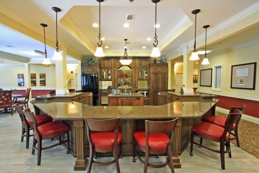 Inviting kitchen with a granite island, red cushioned chairs, dark wood cabinetry, pendant lighting, and a central floral arrangement.