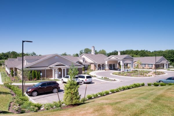 Wide view of a large brick and stone building with multiple entrances, cars parked out front, and manicured lawns.