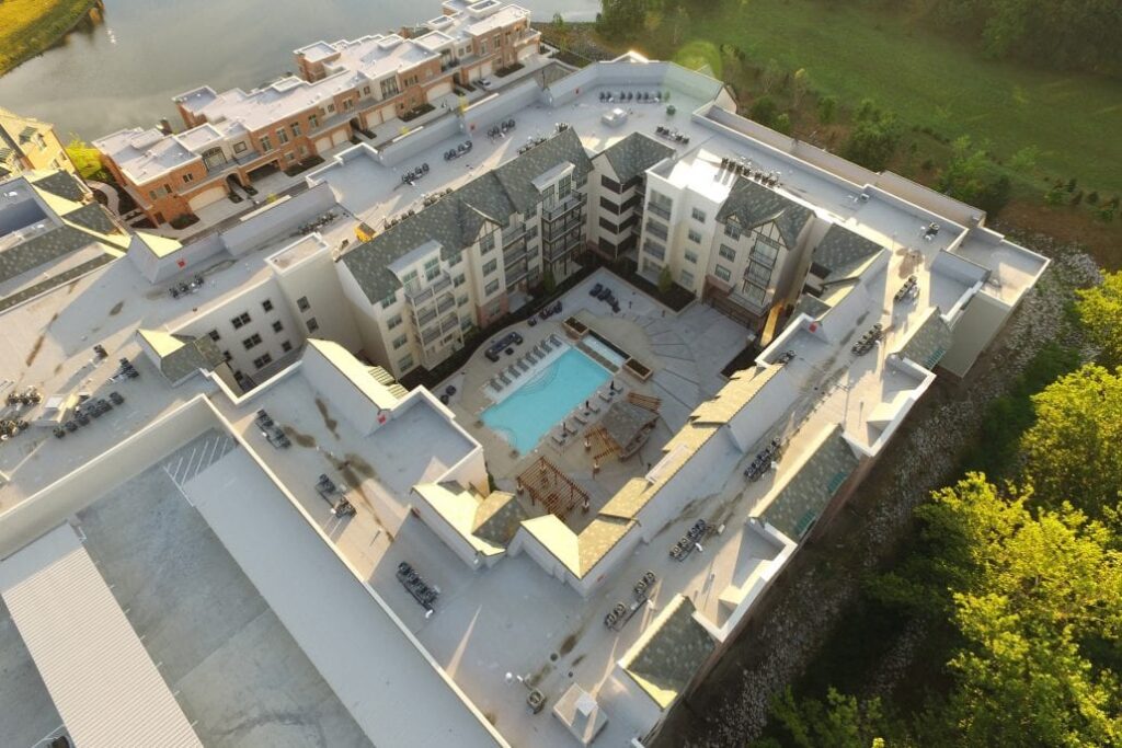 Aerial view of a multi-story residential complex featuring an inner courtyard with a swimming pool, lounge chairs, and pergolas.