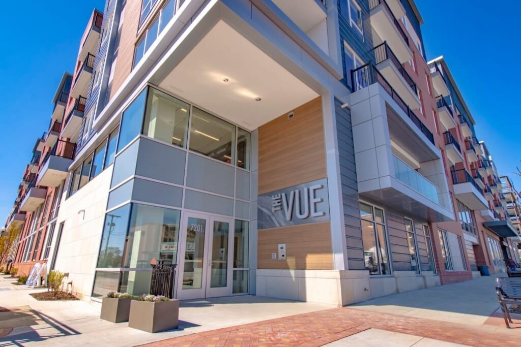 Contemporary multi-story apartment exterior with glass entry, wood accents, balconies, and large 'The Vue' sign.