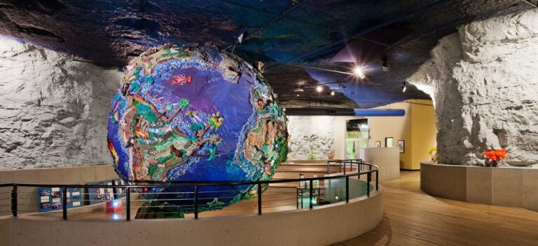 Large decorative globe with detailed artwork displayed inside cave-like rock walls and wooden flooring.