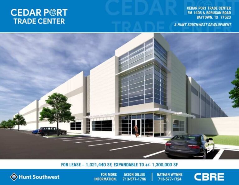 Modern industrial building with tall glass entrance, white façade, and parking spaces under a blue sky.